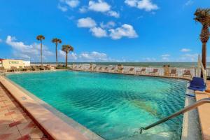 a swimming pool with chairs and palm trees and the ocean at Daytona Beach Resort 532-White Turtle in Daytona Beach