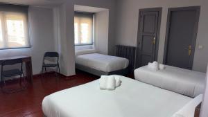 una habitación con dos camas y una mesa y una silla en Hostal La Estación, en Ávila