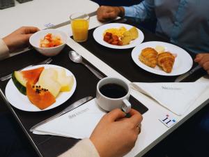 una mesa con platos de comida y una persona sosteniendo una taza de café en Ibis Budget São Bernardo do Campo, en São Bernardo do Campo