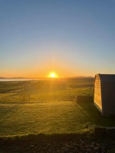 a sunset over a field with a barn at The Orkney Pod in Stromness