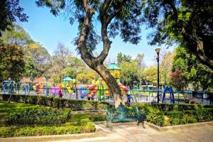 a green park bench with a tree in front of a playground at Suite Rosa familiar para hasta 6 huéspedes Amplia, céntrica, con cocineta y baño privado in Mexico City