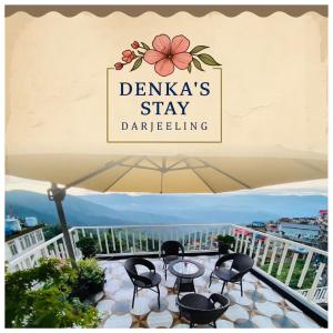 Un cartel en un balcón con sillas y una sombrilla. en Denka's, en Darjeeling