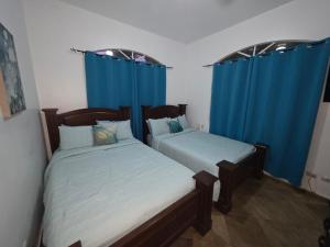 zwei Betten in einem Zimmer mit blauen Vorhängen in der Unterkunft Win Villa in Sosúa + 18 Fotos