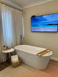 a bathroom with a tub and a tv on the wall at Pousada Cristalmar in Bombinhas
