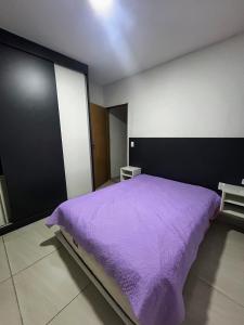 1 Schlafzimmer mit einem lila Bett und 2 Tischen in der Unterkunft Casa aconchegante na Vila Tupi - Perto da Praia in Praia Grande