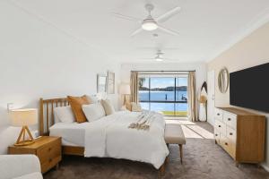 a white bedroom with a large bed and a television at Waters Edge by Coast Hosting in Koolewong