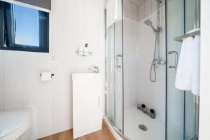 een witte badkamer met douche en wastafel bij Stour Cabin by Tiny Away in Huiroa