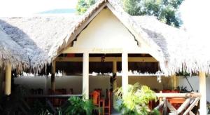 un edificio con techo de paja y un restaurante en Palm Grove Saud Holiday Complex Hotel, en Burayoc