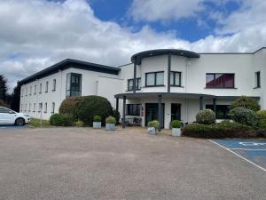 a white building with a car parked in a parking lot at CIT'HOTEL Armony Hotel in Bourg-Achard