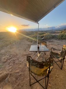 einen Tisch und zwei Stühle mit Sonnenuntergang im Hintergrund in der Unterkunft Palmi Caravan in Poris de Abona