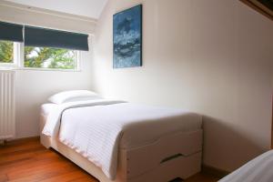 a white bedroom with a bed and a window at Strandbries in Warmenhuizen