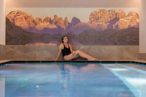 a woman sitting on the edge of a swimming pool at Alpen Hotel Vidi in Madonna di Campiglio