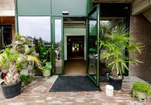 an open glass door of a building with potted plants at De Groene Afslag Kunsthotel in Bussum