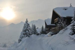 een met sneeuw bedekte hut met de zon op de achtergrond bij Tuschinski in Les Crosets