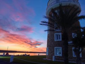 Ein Leuchtturm mit einer Palme vor einem Sonnenuntergang in der Unterkunft Rincon de Almerimar Palm Beach Golf in Almerimar