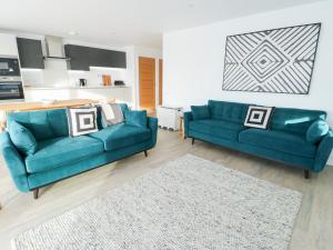 a living room with two blue couches and a kitchen at Glynllifon 4 in Llanallgo