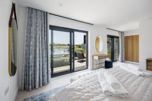 ein Schlafzimmer mit einem großen weißen Bett und einem Balkon in der Unterkunft Knighton - Luxury Dorset lakeside home, sleeps 12 with spa and pool access in Warmwell