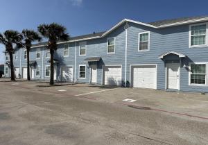 a blue house with two garage doors and palm trees at The Beach Peach in Port Aransas