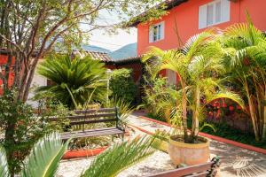 a courtyard with benches and trees and a house at VELINN Pousada Face Norte in Ilhabela