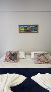 a bed with two pillows and a picture on the wall at Orla Suítes in Porto Seguro