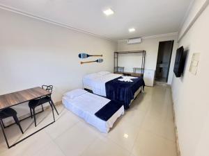 a room with two beds and a table and a desk at Orla Suítes in Porto Seguro
