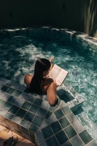 a woman sitting in a swimming pool reading a book at Pousada Maracaju in Porto De Galinhas