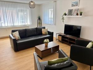 a living room with black leather furniture and a flat screen tv at Visit Oberhof 2 in Oberhof