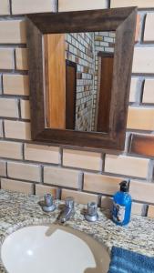 lavabo en el baño con espejo en una pared de ladrillo en Suíte família SOL & LUA Guarda do Embaú SC, en Guarda do Embaú