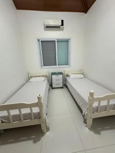 two beds in a white room with a window at Chalés Brisa Do Mar in São Sebastião