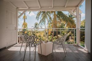 two chairs and a table on a porch with a palm tree at Le M Hotel Marie Galante in Beauregard