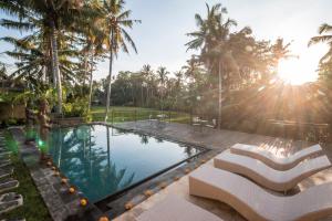 a swimming pool with two white chairs and palm trees at Serenity Villa & Spa in Ubud