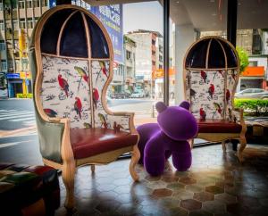 un ours en peluche violet assis à côté de deux chaises dans l'établissement Legend Hotel Kaohsiung Pier2, à Kaohsiung