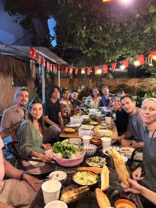 eine Gruppe von Menschen sitzt mit Essen um einen Tisch herum in der Unterkunft Laoxao RiverStone Villa in Hoi An