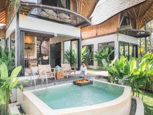 a child standing in front of a house with a swimming pool at Bamboo Asri Ubud in Ubud