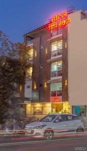 een auto geparkeerd voor een gebouw met een neonbord bij Hotel Girishankara in Indore