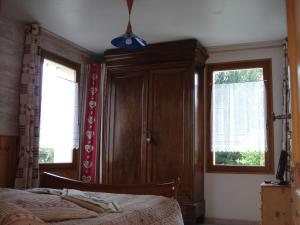 a bedroom with a wooden cabinet and two windows at Le Maurillon in Saint-Pancrace