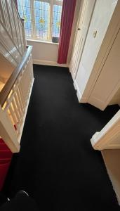 een gang met zwart tapijt en een trap met een raam bij The London Residence in Enfield