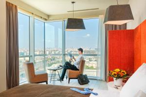 a man sitting in a chair in a room with a large window at Prima Link Hotel in Petaẖ Tiqwa