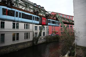 een trein op een brug over een rivier met gebouwen bij ROTH Apartments Wuppertal-HBF in Wuppertal