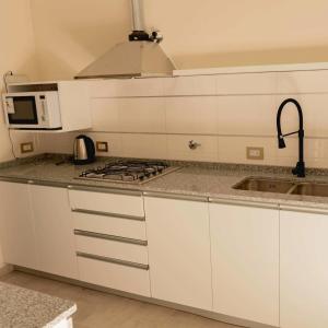 eine Küche mit weißen Schränken und einer Spüle und einer Mikrowelle in der Unterkunft Casabella total confort y relax in Villa Elisa