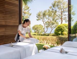 a woman in a white dress standing between two tables at Grand-Hôtel du Cap-Ferrat, A Four Seasons Hotel in Saint-Jean-Cap-Ferrat