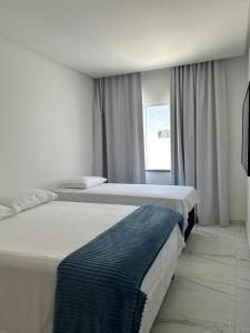 zwei Betten in einem weißen Zimmer mit Fenster in der Unterkunft Casa Brisa do Mar in Lauro de Freitas