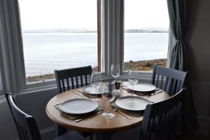 een tafel met stoelen, borden en wijnglazen voor een raam bij Govandale Seaviews in Kingarth