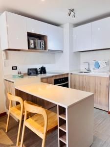 a kitchen with white cabinets and a island with two chairs at Departamento en Península in Iquique