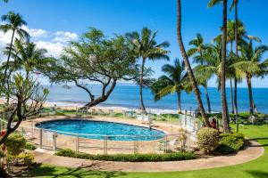a swimming pool with palm trees and the beach at The Hale Pau Hana in Kihei