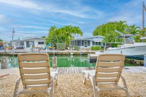 Dos sillas sentadas en un muelle al lado de un barco. en Captain's Cove ~Waterfront Home with Pool & 75' Dock, en Marathon
