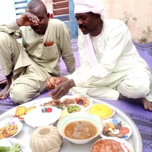 two men sitting on the floor with a plate of food at 4 étoiles in Sarh