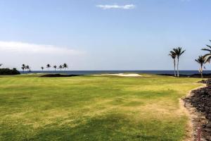 a golf course with palm trees and the ocean at Waikoloa condo with golf & ocean views in Waikoloa