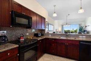 a kitchen with wooden cabinets and a black stove top oven at Spacious 2BR condo with lanai & pool in Waikoloa