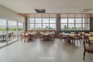 ein Esszimmer mit Tischen, Stühlen und Fenstern in der Unterkunft Apto em Cond. c/ Piscina em Goiânia KSP1304 in Goiânia